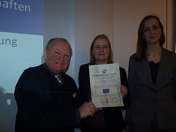 Dietrich Lange (v.l.) erhält die Ehrenurkunde des Instituts für europäische Partnerschaften und internationale Zusammenarbeit (IPZ) von IPZ-Referentin Marijke Mulder. Dazu gratuliert Philippa Saunders, Erste Sekretärin der Britischen Botschaft in Berlin. pr